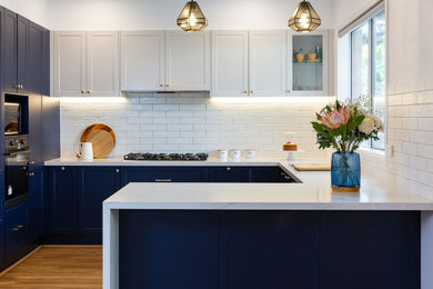 Inspiration for a large modern galley kitchen pantry in Melbourne with a drop-in sink, shaker cabinets, blue cabinets, solid surface benchtops, white splashback, subway tile splashback, stainless steel appliances, medium hardwood floors, with island and white benchtop.
