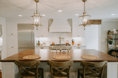 Inspiration for a mid-sized transitional l-shaped open plan kitchen in Atlanta with a farmhouse sink, white cabinets, white splashback, stainless steel appliances, medium hardwood floors, with island, brown floor, recessed-panel cabinets, granite benchtops, ceramic splashback and grey benchtop.