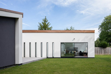 Foto della facciata di una casa grande bianca moderna a un piano con rivestimento in stucco, copertura mista e tetto nero
