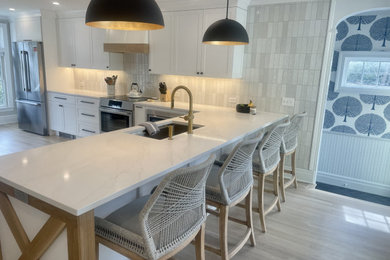 Example of a mid-sized country l-shaped light wood floor kitchen design in New York with an undermount sink, shaker cabinets, white cabinets, quartz countertops, white backsplash, subway tile backsplash, stainless steel appliances, a peninsula and white countertops