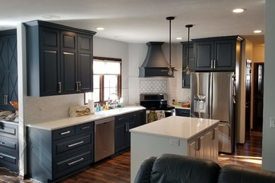 Example of a large u-shaped medium tone wood floor and brown floor kitchen design in Omaha with an undermount sink, raised-panel cabinets, blue cabinets, quartz countertops, white backsplash, stainless steel appliances, an island and white countertops