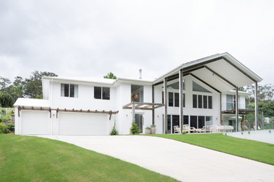 This is an example of a large mediterranean two-storey white house exterior in Sunshine Coast with a metal roof and a white roof.