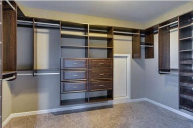 Large trendy gender-neutral carpeted walk-in closet photo in New York with raised-panel cabinets and dark wood cabinets