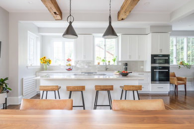 Inspiration for a mid-sized cottage galley medium tone wood floor and exposed beam eat-in kitchen remodel in New York with an undermount sink, white cabinets, quartzite countertops, beige backsplash, ceramic backsplash, stainless steel appliances, an island and beige countertops