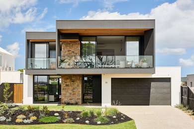 This is an example of a large beach style two-storey black house exterior in Geelong with concrete fiberboard siding, a flat roof and a metal roof.