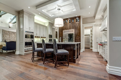 Example of a transitional medium tone wood floor kitchen design in Calgary with raised-panel cabinets, distressed cabinets, stainless steel appliances and an island