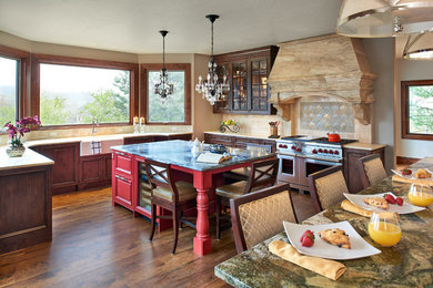 Example of a huge transitional u-shaped medium tone wood floor and brown floor kitchen design in Denver with a farmhouse sink, recessed-panel cabinets, red cabinets, soapstone countertops, beige backsplash, porcelain backsplash, stainless steel appliances and two islands