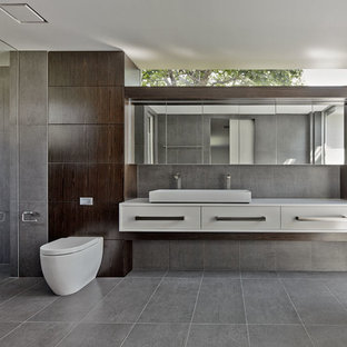 Ispirazione per una stanza da bagno padronale minimalista con ante in legno bruno, vasca freestanding, doccia a filo pavimento, WC sospeso, piastrelle grigie, lavabo rettangolare e pareti marroni