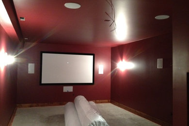 This is an example of a home cinema in Other with red walls, carpet and a projector screen.