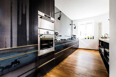 Zweizeilige, Mittelgroße, Offene Moderne Küche ohne Insel mit flächenbündigen Schrankfronten, schwarzen Schränken, braunem Holzboden, Arbeitsplatte aus Holz, Küchenrückwand in Grau, Küchengeräten aus Edelstahl, integriertem Waschbecken und braunem Boden in München