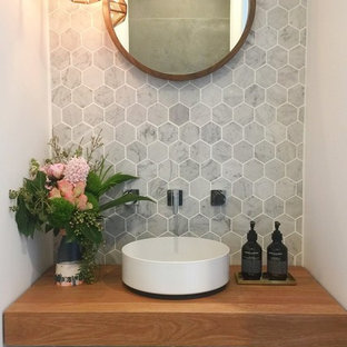 Ispirazione per un piccolo bagno di servizio moderno con WC sospeso, piastrelle grigie, piastrelle di marmo, pareti bianche, pavimento in gres porcellanato, lavabo a bacinella, top in legno, pavimento grigio e top marrone