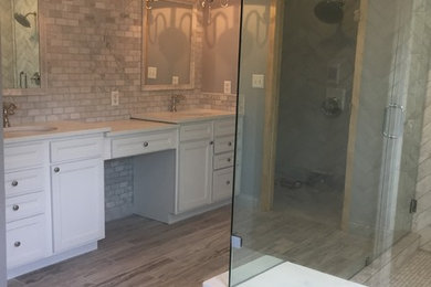 Photo of a mid-sized transitional master bathroom in Little Rock with white cabinets, a corner shower, gray tile, stone tile, grey walls, ceramic floors, an undermount sink, a hinged shower door, beige floor, recessed-panel cabinets and white benchtops.