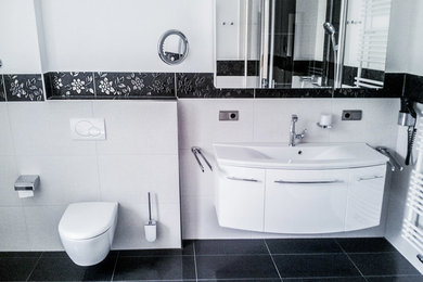 Großes Modernes Duschbad mit flächenbündigen Schrankfronten, weißen Schränken, bodengleicher Dusche, Wandtoilette mit Spülkasten, Keramikfliesen, weißer Wandfarbe, Keramikboden, Unterbauwaschbecken, Waschtisch aus Holz, schwarzem Boden, Falttür-Duschabtrennung und weißer Waschtischplatte in Essen
