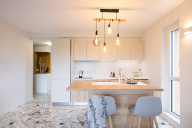 Idée de décoration pour une cuisine ouverte bicolore et linéaire design de taille moyenne avec un placard à porte affleurante, des portes de placard beiges, un plan de travail en stratifié, îlot, un évier encastré, une crédence blanche, une crédence en céramique, un électroménager noir, un sol en marbre, un plan de travail blanc et un sol gris.