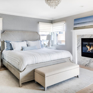 Inspiration for a mid-sized beach style master bedroom in Los Angeles with grey walls, light hardwood floors, a standard fireplace, a stone fireplace surround and beige floor.