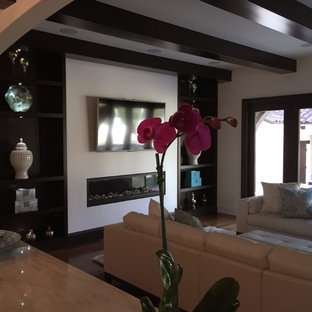 Mittelgroßes, Abgetrenntes, Repräsentatives Mediterranes Wohnzimmer mit weißer Wandfarbe, braunem Holzboden, Gaskamin, verputztem Kaminsims, Wand-TV und braunem Boden in Tampa