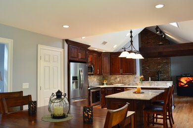 Mid-sized minimalist l-shaped light wood floor eat-in kitchen photo in New York with a single-bowl sink, raised-panel cabinets, dark wood cabinets, quartzite countertops, gray backsplash, stone tile backsplash, stainless steel appliances and an island