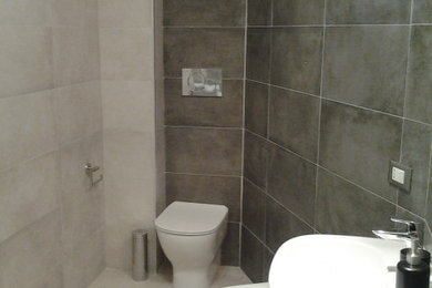 This is an example of a mid-sized contemporary powder room in Other with a two-piece toilet, gray tile, porcelain tile, white walls, porcelain floors, a wall-mount sink and grey floor.