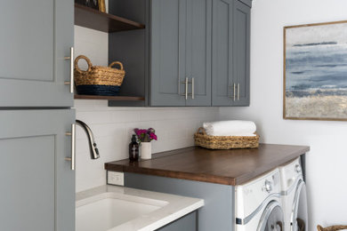 ボストンにあるトランジショナルスタイルのおしゃれな洗濯室 (I型、アンダーカウンターシンク、青いキャビネット、クオーツストーンカウンター、白いキッチンパネル、サブウェイタイルのキッチンパネル、白い壁、セラミックタイルの床、左右配置の洗濯機・乾燥機、白いキッチンカウンター) の写真