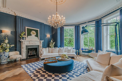 This is an example of an expansive traditional open concept living room in London with blue walls, a standard fireplace, a stone fireplace surround, no tv and medium hardwood floors.