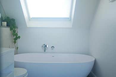 Medium sized modern ensuite bathroom in Surrey with freestanding cabinets, white cabinets, a freestanding bath, a walk-in shower, a wall mounted toilet, beige tiles, porcelain tiles, beige walls, porcelain flooring, a wall-mounted sink, engineered stone worktops, grey floors, an open shower and white worktops.