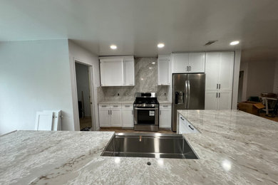 Eat-in kitchen - tropical light wood floor and beige floor eat-in kitchen idea in Dallas with quartz countertops, a farmhouse sink, shaker cabinets, white cabinets, beige backsplash, quartz backsplash, stainless steel appliances, an island and beige countertops