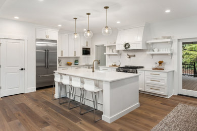 Inspiration for a transitional l-shaped brown floor and medium tone wood floor kitchen remodel in Atlanta with a farmhouse sink, white cabinets, white backsplash, ceramic backsplash, an island, shaker cabinets, stainless steel appliances and white countertops