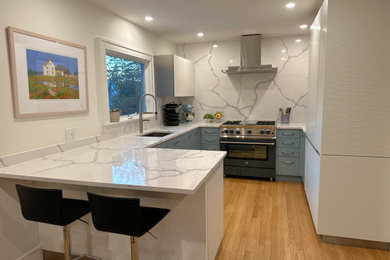 Inredning av ett modernt litet vit vitt kök, med en undermonterad diskho, släta luckor, blå skåp, bänkskiva i kvarts, vitt stänkskydd, rostfria vitvaror, ljust trägolv, en halv köksö och beiget golv