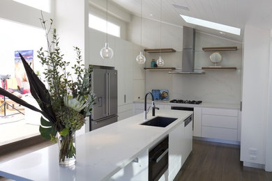 This is an example of a large modern galley separate kitchen in Sydney with an undermount sink, flat-panel cabinets, white cabinets, quartz benchtops, white splashback, stone slab splashback, black appliances, light hardwood floors, with island, brown floor and white benchtop.