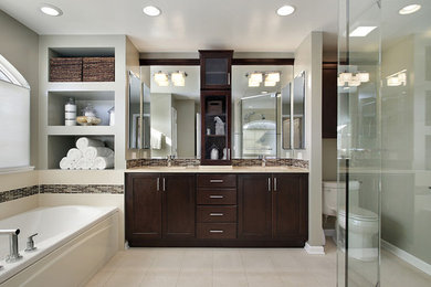 Inspiration for a large traditional master bathroom in New Orleans with recessed-panel cabinets, dark wood cabinets, a drop-in tub, a corner shower, a one-piece toilet, grey walls, porcelain floors, an undermount sink, beige floor, ceramic tile, solid surface benchtops, a hinged shower door and beige benchtops.