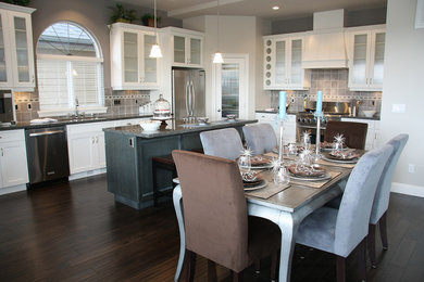 Example of a mid-sized classic l-shaped dark wood floor and brown floor eat-in kitchen design in Tampa with stainless steel appliances, an undermount sink, glass-front cabinets, white cabinets, granite countertops, gray backsplash, an island and ceramic backsplash