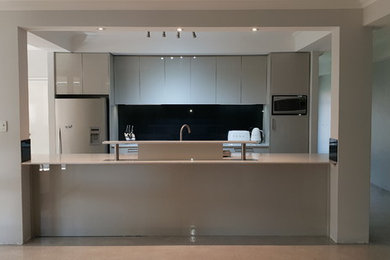 Inspiration for a mid-sized contemporary galley eat-in kitchen in Perth with a double-bowl sink, glass-front cabinets, beige cabinets, quartz benchtops, black splashback, glass sheet splashback, stainless steel appliances, concrete floors, with island, grey floor and white benchtop.