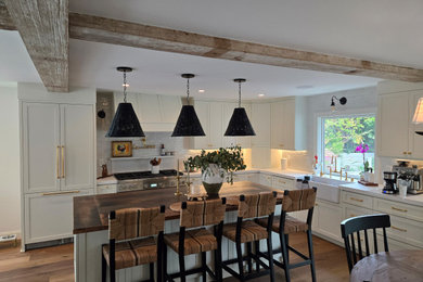 Beach style brown floor and exposed beam eat-in kitchen photo in Orange County with white cabinets, wood countertops, white backsplash, subway tile backsplash, stainless steel appliances, an island and brown countertops