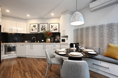 Small modern u-shaped open plan kitchen in Melbourne with a double-bowl sink, flat-panel cabinets, white cabinets, quartz benchtops, black splashback, ceramic splashback, stainless steel appliances, laminate floors, no island, brown floor and white benchtop.