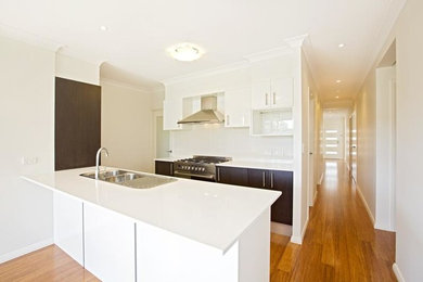 Photo of a small modern galley eat-in kitchen in Sydney with a double-bowl sink, raised-panel cabinets, dark wood cabinets, quartz benchtops, white splashback, ceramic splashback, stainless steel appliances, bamboo floors and with island.