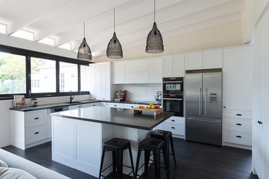 This is an example of a large country kitchen in Brisbane with an undermount sink, shaker cabinets, white cabinets, quartz benchtops, white splashback, ceramic splashback, laminate floors, with island, black floor and black benchtop.