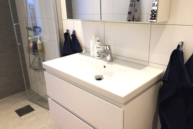 This is an example of a medium sized scandinavian shower room bathroom in Other with flat-panel cabinets, white cabinets, a walk-in shower, a wall mounted toilet, white tiles, cement tiles, white walls, cement flooring, a wall-mounted sink, beige floors and a hinged door.