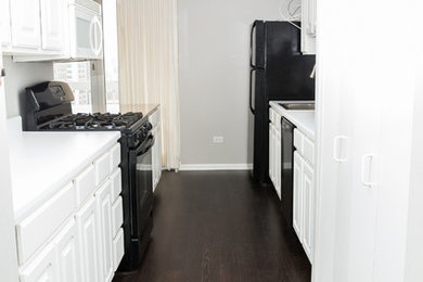 Enclosed kitchen - small modern galley dark wood floor and brown floor enclosed kitchen idea in Chicago with a drop-in sink, raised-panel cabinets, white cabinets, solid surface countertops and black appliances