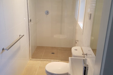 ニューカッスルにあるお手頃価格の広いモダンスタイルのおしゃれな浴室 (アルコーブ型シャワー、分離型トイレ、白いタイル、セメントタイル、白い壁、セメントタイルの床、一体型シンク、茶色い床、開き戸のシャワー) の写真