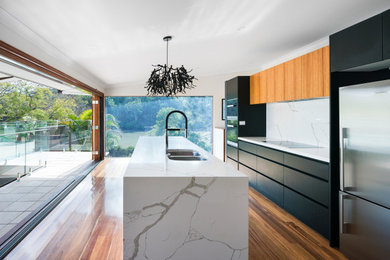 Design ideas for a mid-sized contemporary galley open plan kitchen in Brisbane with an undermount sink, white cabinets, quartz benchtops, white splashback, marble splashback, stainless steel appliances, medium hardwood floors, with island and white benchtop.
