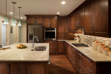 Example of a mid-sized classic l-shaped medium tone wood floor and brown floor kitchen design in Charlotte with an undermount sink, flat-panel cabinets, dark wood cabinets, quartzite countertops, beige backsplash, glass tile backsplash, stainless steel appliances, an island and beige countertops