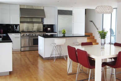 Inspiration for a mid-sized contemporary l-shaped light wood floor eat-in kitchen remodel in Orange County with flat-panel cabinets, white cabinets, solid surface countertops, black backsplash, stone slab backsplash, stainless steel appliances and an island