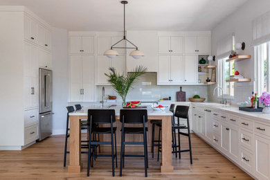 Inspiration for a mid-sized contemporary kitchen in San Francisco with a single-bowl sink, shaker cabinets, white cabinets, quartz benchtops, white splashback, glass tile splashback, stainless steel appliances, light hardwood floors, with island and white benchtop.