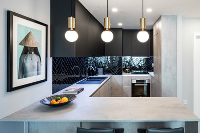 This is an example of a small contemporary u-shaped open plan kitchen in Dublin with an integrated sink, flat-panel cabinets, black cabinets, laminate benchtops, black splashback, ceramic splashback, black appliances, medium hardwood floors, a peninsula, beige floor and grey benchtop.