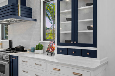 Huge beach style medium tone wood floor and brown floor eat-in kitchen photo in Miami with a farmhouse sink, shaker cabinets, white cabinets, quartzite countertops, gray backsplash, subway tile backsplash, stainless steel appliances, two islands and white countertops