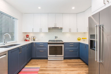 Example of a transitional medium tone wood floor kitchen design in Vancouver with an undermount sink, shaker cabinets, blue cabinets, quartz countertops, white backsplash, ceramic backsplash, stainless steel appliances and white countertops