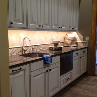 This is an example of a mid-sized transitional single-wall kitchen pantry in Boise with a single-bowl sink, raised-panel cabinets, white cabinets, beige splashback, ceramic splashback, stainless steel appliances, porcelain floors and brown floor.