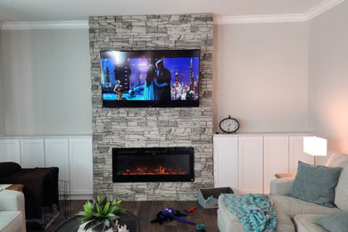 デンバーにあるおしゃれなファミリールーム (白い壁、標準型暖炉、積石の暖炉まわり、壁掛け型テレビ) の写真