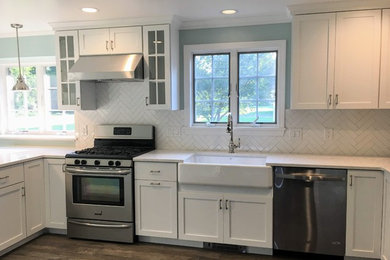 Photo of a mid-sized transitional u-shaped separate kitchen in Boston with a farmhouse sink, shaker cabinets, white cabinets, granite benchtops, white splashback, porcelain splashback, stainless steel appliances, dark hardwood floors, a peninsula, brown floor and white benchtop.