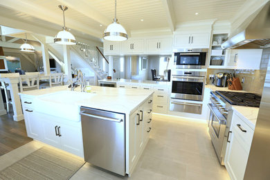 Large trendy l-shaped beige floor kitchen photo in Other with a farmhouse sink, shaker cabinets, white cabinets, marble countertops, brown backsplash, glass tile backsplash, stainless steel appliances and an island